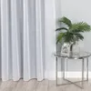 A white sheer curtain hangs on the left side of the image, with a small round glass table on the right. The table has a silver pineapple-shaped vase with green palm leaves and a framed photo on it. Produktbild-Vorschau