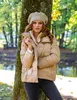 A woman wearing a beige puffer jacket and a matching beret stands next to a tree in a park during autumn. Anteprima dell’immagine prodotto