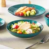 A close-up shot of a salad in a teal bowl, with another plate of shrimp and vegetables in the background. Produktbild-Vorschau