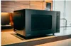 A black Panasonic microwave oven is placed on a wooden countertop in a kitchen. Anteprima dell’immagine prodotto