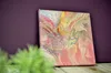 A painting with abstract swirls of color is displayed on a wooden surface against a purple wall. Green foliage is blurred in the foreground. Voir les images du produit