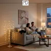 A couple sits on a couch in a living room, looking at a tablet. A decorative tree with lights is in the foreground. Podgląd zdjęcia produktu