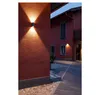 An outdoor wall light illuminates a textured red wall and a cobblestone pathway next to a building. Produktbild-Vorschau