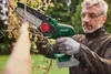 A man is using a cordless chainsaw to cut a branch in an outdoor setting. Produktbild-Vorschau