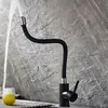 A black kitchen faucet with a flexible hose is shown with water running from it, against a textured gray tile background. A lemon and a white cup are visible in the foreground. Náhľad obrázku produktu
