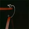 A close-up of a silver cat-shaped bag hook hanging from the edge of a wooden table, with a brown leather bag strap attached. Anteprima dell’immagine prodotto