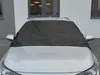 A black car windshield cover is placed on the front windshield of a silver car, parked in front of a building. Náhled obrázku produktu