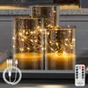 Three glass cylinders with integrated LED string lights, a USB charging cable, and a remote control. Produktbild-Vorschau
