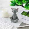 A meditating cat figurine sits on a desk next to a candle and a keyboard, with a small potted plant in the background. Produktbild-Vorschau