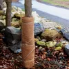 A tree trunk wrapped in brown material, surrounded by rocks and fallen leaves. Voir les images du produit