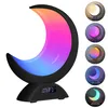 A crescent moon-shaped lamp with a gradient of colors, displaying a digital clock on its base. Several smaller circular images of the lamp showing different color settings are arranged to its right. Produktbild-Vorschau