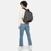 A woman wearing a cream sweater and blue jeans stands with her back to the camera, wearing a gray Eastpak Wyoming Black Denim Rucksack. Produktbild-Vorschau