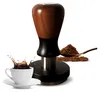 A coffee tamper with a wooden handle, placed next to a cup of coffee and a spoon of coffee grounds. Náhled obrázku produktu