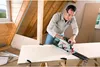 A man is using a Bosch circular saw to cut a piece of wood in an attic. Podgląd zdjęcia produktu