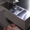 A close-up shot of a sewing machine needle and presser foot, with a hand adjusting a part of the machine. Náhled obrázku produktu