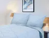 A close-up view of a bed with light blue bedding and pillows, set against a white wall with a framed picture above. Podgląd zdjęcia produktu