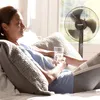 A woman is relaxing in bed with a book and a glass of water, a fan is running in the background. Produktbild-Vorschau