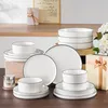 A collection of white ceramic dishes with black rim stripes, arranged on a wooden surface, with decorative items in the background. Náhled obrázku produktu