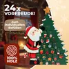 A Christmas advent calendar shaped like a Christmas tree with Santa Claus next to it, set against a festive background with fireplace and Christmas lights. Produktbild-Vorschau