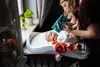A woman is holding a baby book over a baby lying on a changing table. Toys are also on the changing table. Anteprima dell’immagine prodotto