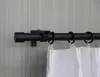 A close-up view of a black curtain rod mounted on a textured wall, with white curtains attached via rings. Produktbild-Vorschau