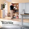 A man is standing in a room with bookshelves and a desk, holding a book. Produktbild-Vorschau