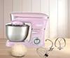 A pink stand mixer with stainless steel bowl and attachments on a wooden surface with a light wood paneled background. Produktbild-Vorschau