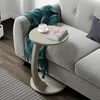 A C-shaped side table with a book and coffee cup on it, placed next to a sofa with a teal throw blanket. Voir les images du produit
