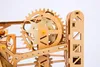 A close-up view of a wooden mechanical model, likely a marble run or similar construction kit, showing gears and structural components. Voir les images du produit
