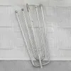 A close-up view of several metal curtain hooks resting on a white textured fabric. Náhled obrázku produktu
