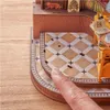A close-up view of a miniature wooden book nook with a detailed tiled floor and a finger pointing at the edge. Náhled obrázku produktu