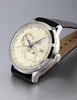 A close-up studio shot of a men's wristwatch with a cream-colored dial and a brown leather strap, set against a light gray background. Produktbild-Vorschau