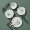 A top-down view of four plates with a floral design, arranged on a green surface with a sprig of eucalyptus and cutlery. Produktbild-Vorschau