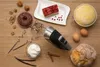 A collection of baking ingredients and a hand mixer are arranged on a wooden surface. Produktbild-Vorschau