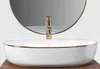 A close-up shot of a white oval countertop sink with a gold rim and a gold faucet, reflected in a round mirror behind it. Náhled obrázku produktu