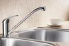 A chrome kitchen faucet is shown above a stainless steel sink, with a white teacup and saucer on the countertop in the background. Produktbild-Vorschau