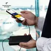 A person is holding a smartphone and a power bank in an airport setting. Náhľad obrázku produktu
