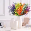 A bouquet of artificial flowers in various vibrant colors is displayed in a white vase on a table, with two smaller white vases and a candle holder nearby. Produktbild-Vorschau
