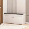 A white shoe cabinet with a black top and a single drawer is shown in a room with a wooden door and a rug. Podgląd zdjęcia produktu