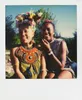 Two women are sitting outdoors, smiling at the camera. They are both wearing traditional African clothing and jewelry. Produktbild-Vorschau