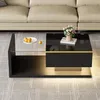 A modern black coffee table with a glass top, featuring LED lighting and a decorative flower arrangement, placed in a living room setting. Produktbild-Vorschau