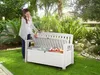 A woman is opening a white storage bench in a garden setting. Náhľad obrázku produktu
