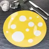 A yellow plate with white polka dots is shown on a dark gray slate surface, with cutlery and a small jar in the background. Podgląd zdjęcia produktu