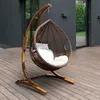 A hanging chair with cushions on a wooden deck in front of a modern building. Produktbild-Vorschau