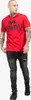 A man wearing a red t-shirt and black jeans, standing against a white background. Produktbild-Vorschau