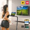 A woman is running on a treadmill in a modern living room, with a large TV screen displaying a scenic view and a smartphone showing an app. Podgląd zdjęcia produktu