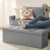 A person is reading a book while resting their feet on a storage ottoman in front of a sofa. Náhled obrázku produktu