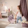 A young girl is playing with a doll stroller in a bedroom. Náhled obrázku produktu
