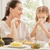 A mother and daughter are having breakfast, with the daughter drinking milk and the mother looking at her. Produktbild-Vorschau