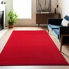 A red rug is laid out on a wooden floor in a living room, with a blue sofa and a cabinet in the background. Podgląd zdjęcia produktu